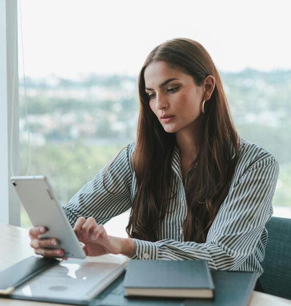 Young elegant woman sits at a desk and interacts with a tablet